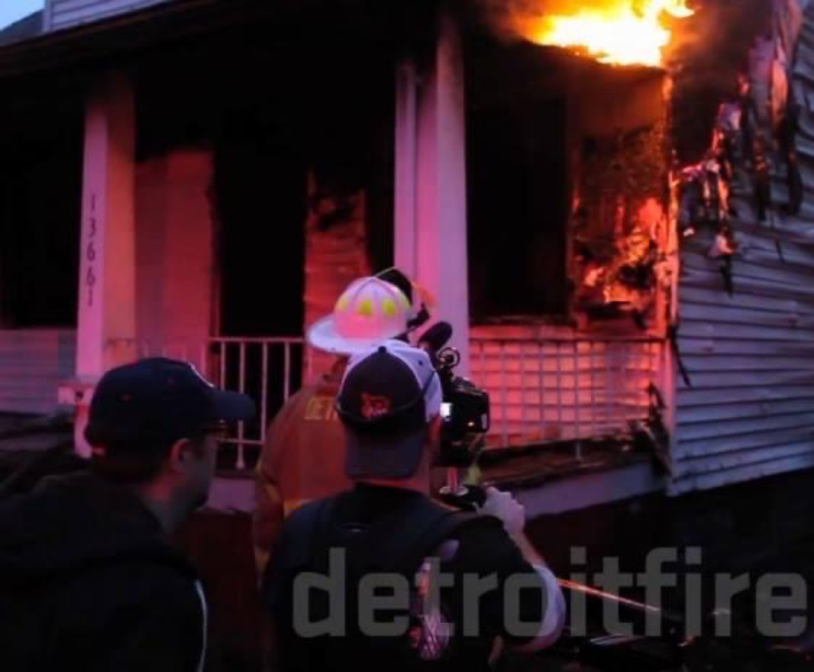 Firefighters and a camera operator outside a burning house during BURN